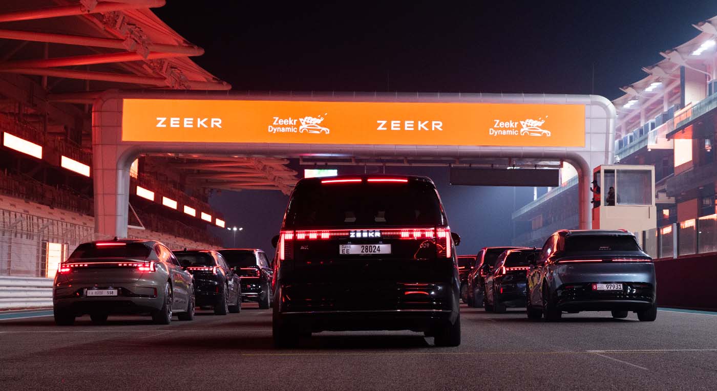 Luxury electric cars lined up at night on a race track under a large glowing orange Zeekr Dynamic archway
